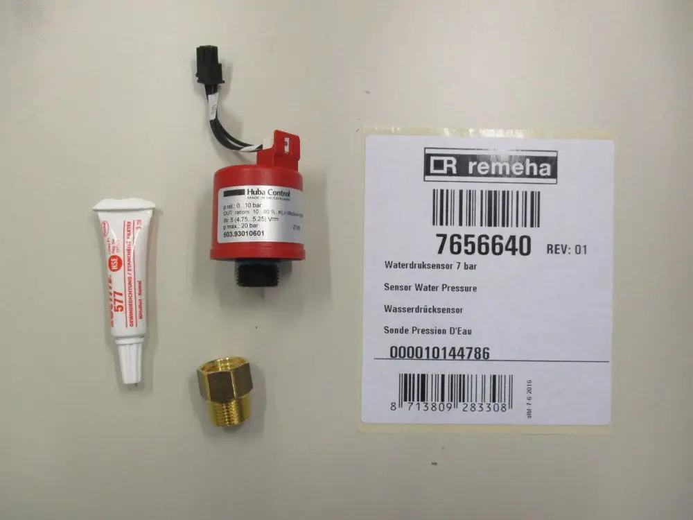 Remeha Wasserdrucksensor mit Anschluss, einer Montagepaste und einer Metallverbindung, auf einem hellen Hintergrund. Verpackung mit Artikelnummer und weiteren Informationen ist sichtbar.